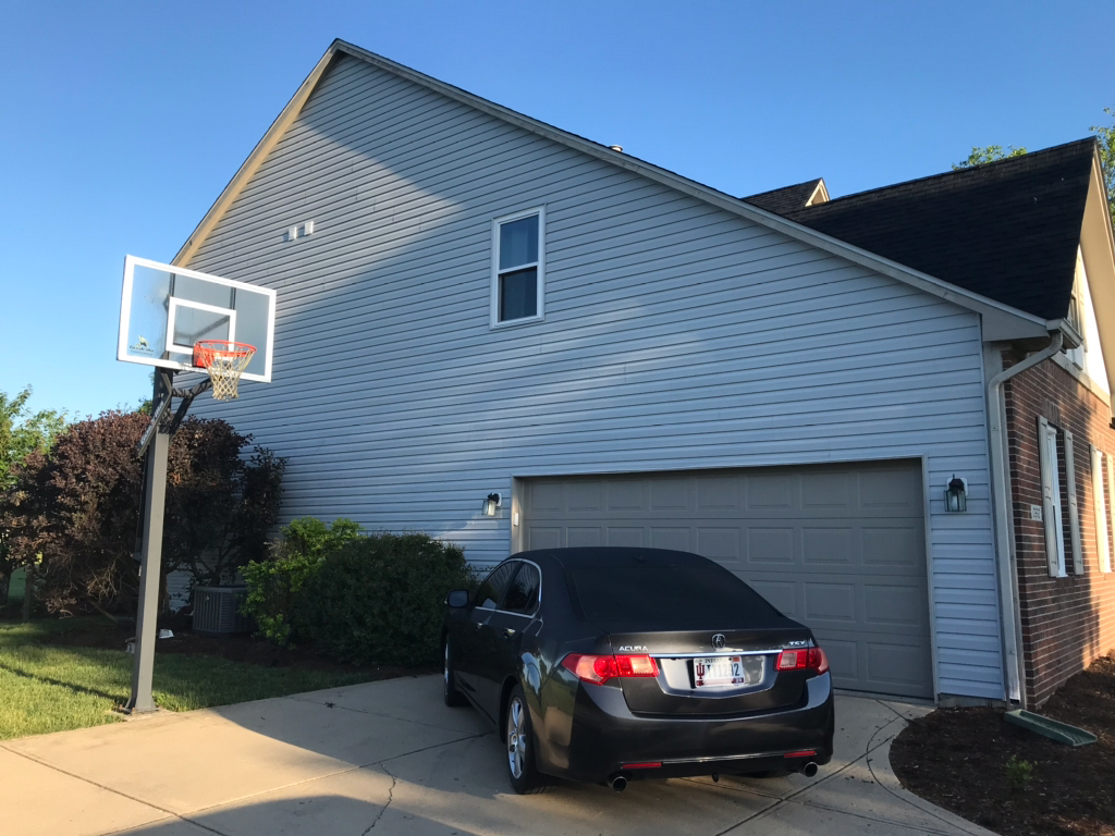View of home with new fiber cement siding, a basketball hoop, and car in front of garage